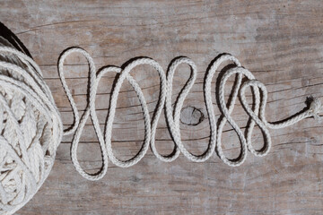 A huge ball of natural cotton rope of a milky color on a wooden board, the cord is lined with a zigzag, top view