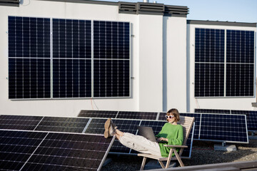 Woman works on laptop and phone while sitting on rooftop with a solar station. Concept of remote...