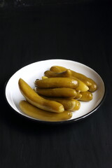 Cucumber pickles in a plate on a black background