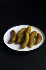 Cucumber pickles in a plate on a black background