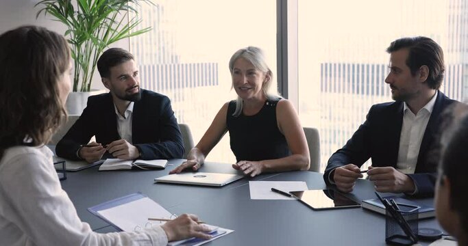 Mature businesswoman, business coach lead corporate training for staff sit together at desk in modern boardroom, share information, make speech for partners, take part in formal negotiations in office