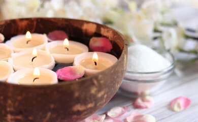 Obraz na płótnie Canvas Burning candles in water. Spa composition with coconut bowl, rose petals. Rest, relaxation, composition for a massage room