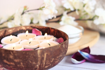 Burning candles in water. Spa composition with coconut bowl, rose and tulip petals. Rest, relaxation, composition for a massage room