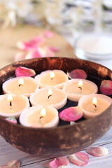Burning candles in water. Spa composition. Coconut bowl with candles and rose petals, flowers and a blurred background. Vertical photo.