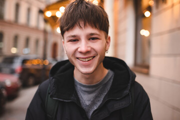 Funny smiling teenage boy 17-18 year old with blond hair wearing hoodie walking in city street...