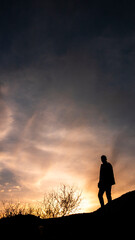 Fototapeta premium Men raise their arms in sunrise,Landscape with silhouette of a standing happy man with backpack and raised-up arms on the mountain peak on the background of cloudy sky at colorful sunset