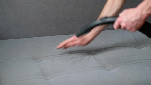 dusting a gray sofa with a vacuum cleaner and dry air