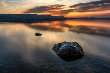 Bodensee Seeufer mit Steinen im Wasser kraftvoller Sonnenuntergang mit schönen Farben am Himmel 