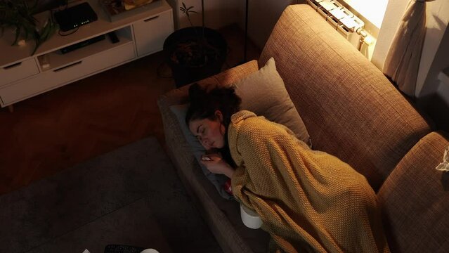 On sick leave. Suffering Caucasian woman is lying on sofa with handkerchief, covered with blanket. Top view. Cold and illness.