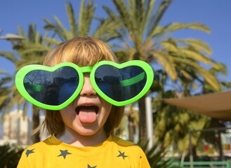 A cute boy in large glasses in the shape of a heart. The child rejoices in the holiday. Concept:...