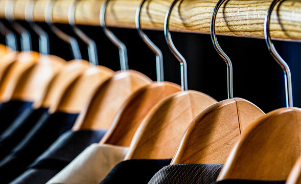 Mens suits in different colors hanging on hanger in a retail clothes store, close-up. Mens shirts, suit hanging on rack. Hangers with jackets on them in boutique. Suits for men hanging on the rack