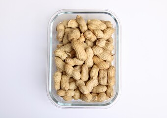 Glass dish of peanuts or monkey nuts against plain white background