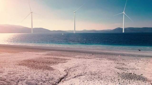 Aerial view of 3 massive wind turbines in the sea.