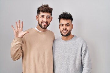 Young homosexual couple standing over white background showing and pointing up with fingers number five while smiling confident and happy.