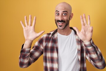 Hispanic man with beard standing over yellow background showing and pointing up with fingers number...