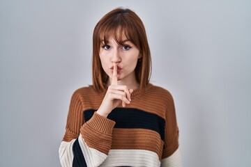 Young beautiful woman wearing striped sweater over isolated background asking to be quiet with...