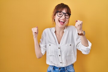 Young beautiful woman wearing casual shirt over yellow background celebrating surprised and amazed for success with arms raised and eyes closed. winner concept.