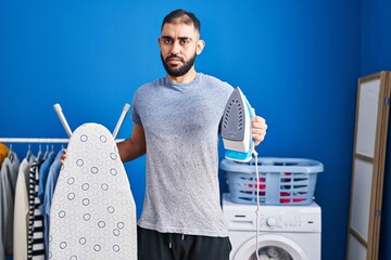 Middle east man with beard holding electric iron clueless and confused expression. doubt concept.