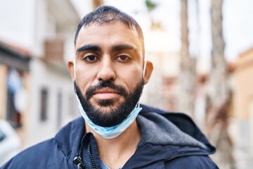 Young hispanic man wearing medical mask standing at street