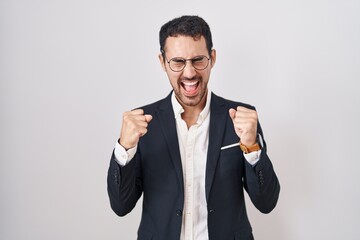 Handsome business hispanic man standing over white background excited for success with arms raised and eyes closed celebrating victory smiling. winner concept.