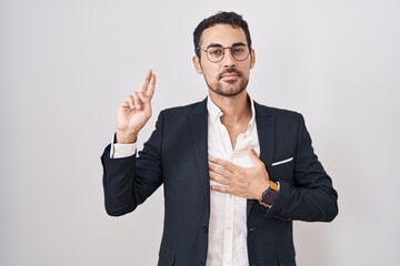 Handsome business hispanic man standing over white background smiling swearing with hand on chest and fingers up, making a loyalty promise oath - obrazy, fototapety, plakaty