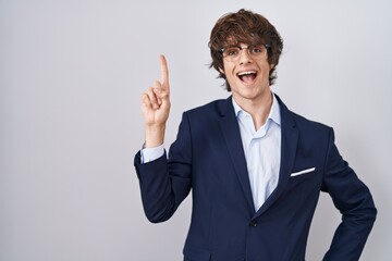 Hispanic business young man wearing glasses pointing finger up with successful idea. exited and happy. number one.