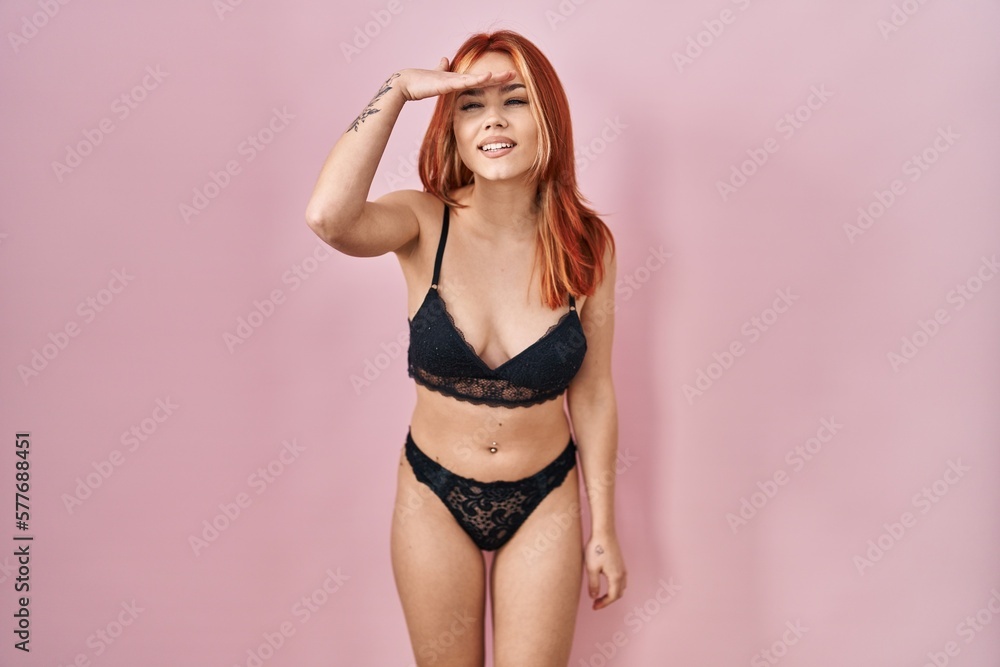 Canvas Prints Young caucasian woman wearing lingerie over pink background very happy and smiling looking far away with hand over head. searching concept.