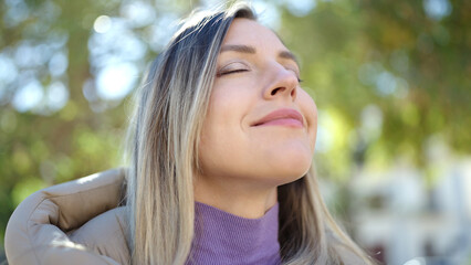 Naklejka premium Young blonde woman breathing with closed eyes at park