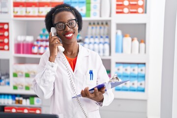 African american woman pharmacist talking on telephone reading document at pharmacy