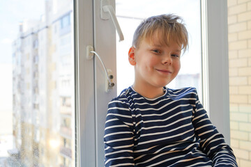 safety at home for small children. a lock on the window protects children from opening the window. The boy is sitting on the window on a high floor.