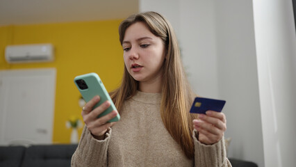 Young blonde woman using smartphone and credit card sitting on floor at home