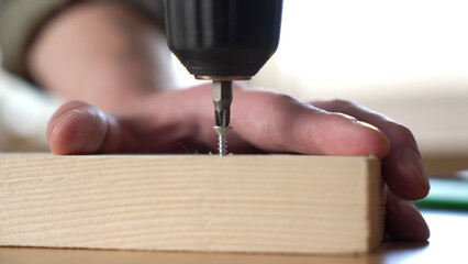 male craftsman screwing a self-tapping screw into a board with a screwdriver.