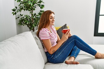 Young woman drinking coffee sitting on sofa at home