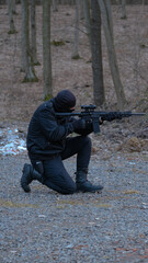 A soldier of a special unit in a black uniform shoots an assault rifle at a training ground