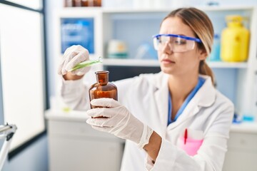 Young hispanic woman scientist pouring liquid on bottle at laboratory