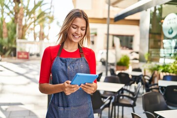 Young hispanic woman waitress smiling confident using touchpad at coffee shop terrace