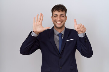 Young hispanic business man wearing suit and tie showing and pointing up with fingers number six while smiling confident and happy.