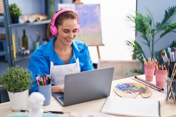 Young woman artist using laptop and headphones at art studio
