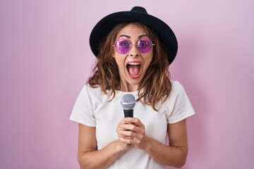 Beautiful brunette woman singing song using microphone celebrating crazy and amazed for success...