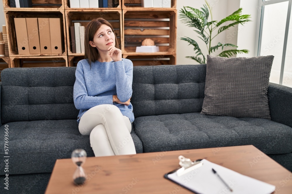 Sticker young brunette woman at consultation office with hand on chin thinking about question, pensive expre