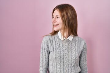 Beautiful woman standing over pink background looking away to side with smile on face, natural expression. laughing confident.