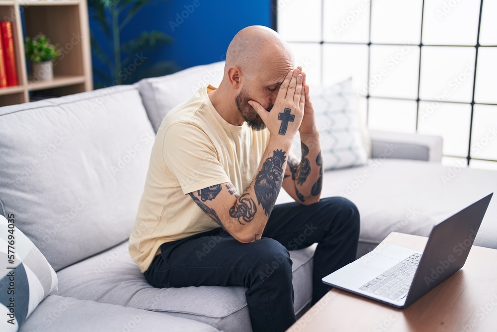 Sticker young bald man stressed using laptop sitting on sofa at home