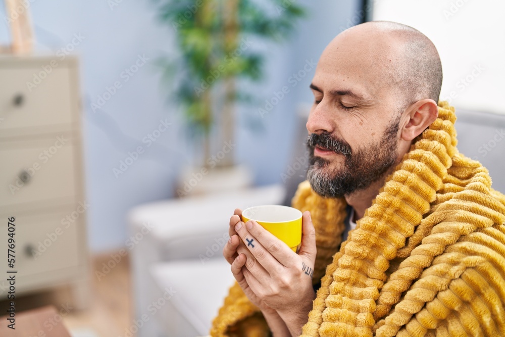 Poster Young bald man drinking coffee sitting on sofa at home