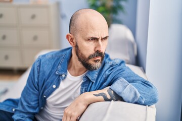 Young bald man sitting on sofa with serious expression at home