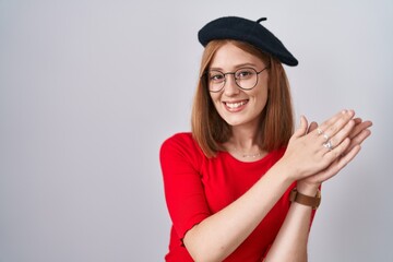 Young redhead woman standing wearing glasses and beret clapping and applauding happy and joyful, smiling proud hands together