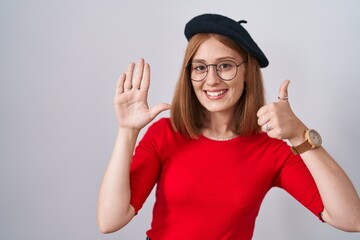 Obraz na płótnie Canvas Young redhead woman standing wearing glasses and beret showing and pointing up with fingers number six while smiling confident and happy.