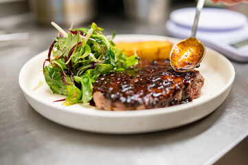 professional chef's hands cooking Grilled Ribeye Steak on plate with Potato gratin and salad in...