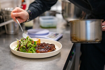 professional chef's hands cooking Grilled Ribeye Steak on plate with Potato gratin and salad in restaurant kitchen