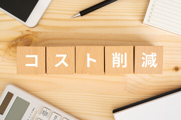 コスト削減と書かれたブロック、電卓、スマホ、カレンダー、ノート
