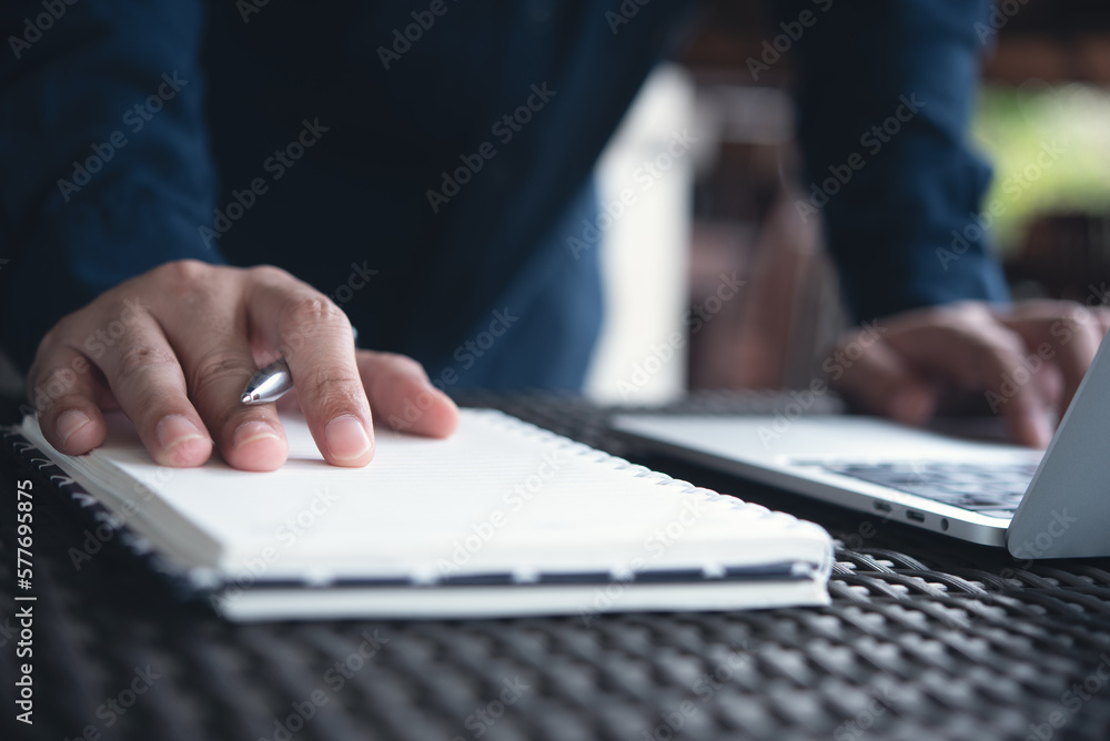 Wall mural Business man hand writing on notepad, working on laptop computer on table at coffee shop. Student studying online, planning, searching internet and note ideas on notebook